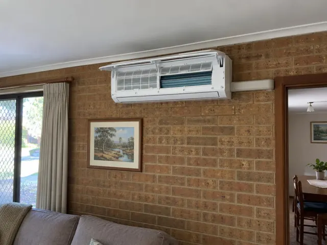 Clean indoor split system on a brick wall with open front panel and visible filters in a lounge in Clearview