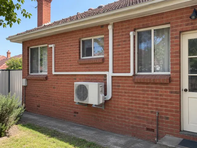 Brick home exterior with one wall-mounted outdoor unit and white pipe covers running to several rooms in Prospect