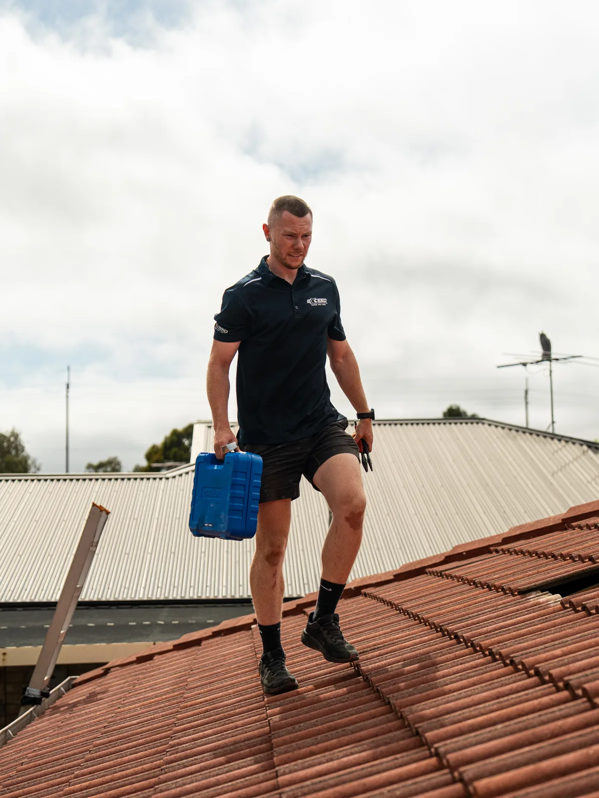 Technician crossing a tiled roof with a toolbox